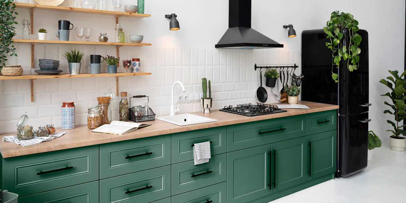 Bucătărie modernă cu dulapuri verde închis, electrocasnice retro negre și rafturi deschise din lemn, oferind un aer proaspăt și organizat.